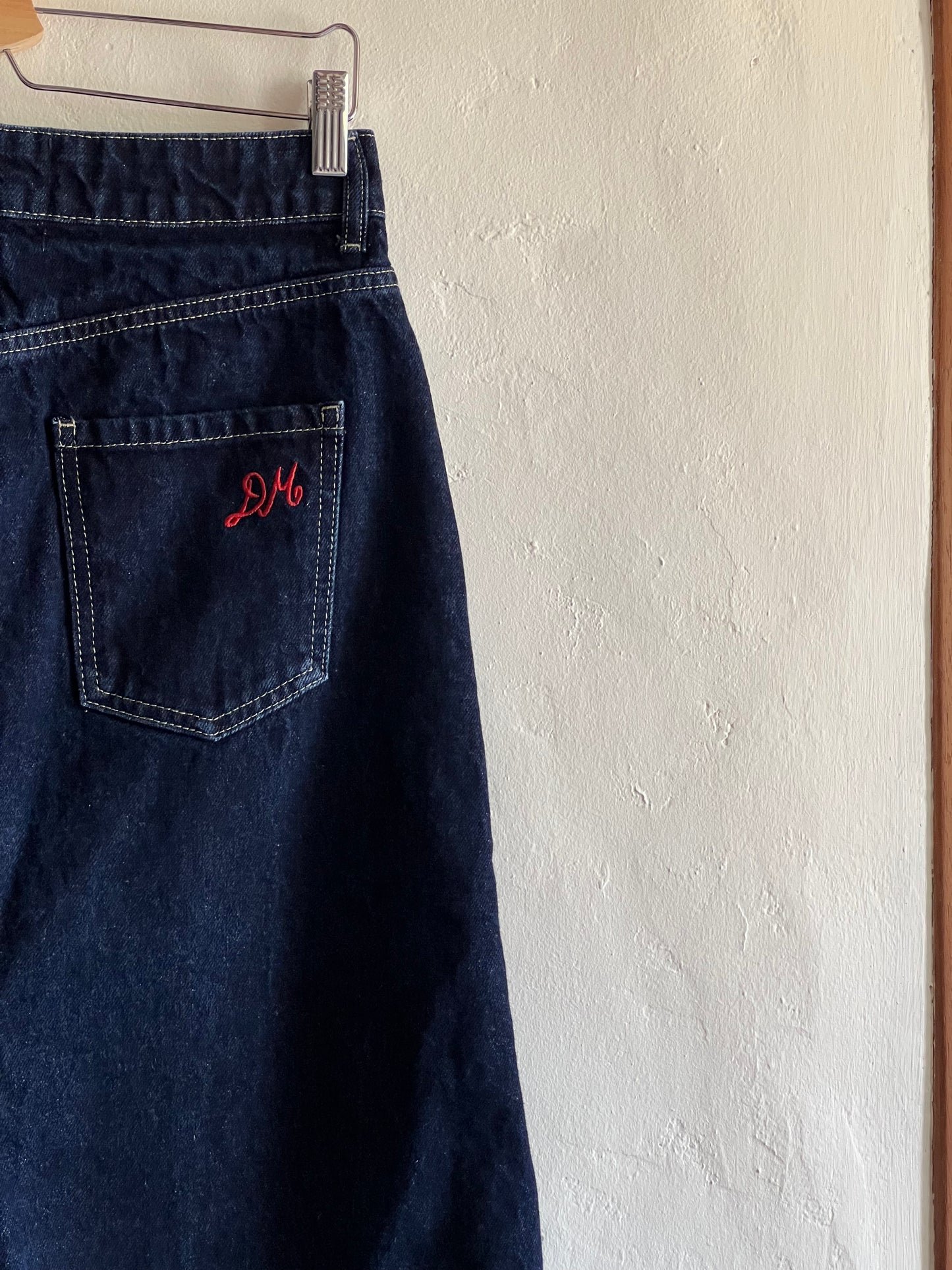 Damson Madder Dark Denim Midi Skirt hanging against a white wall