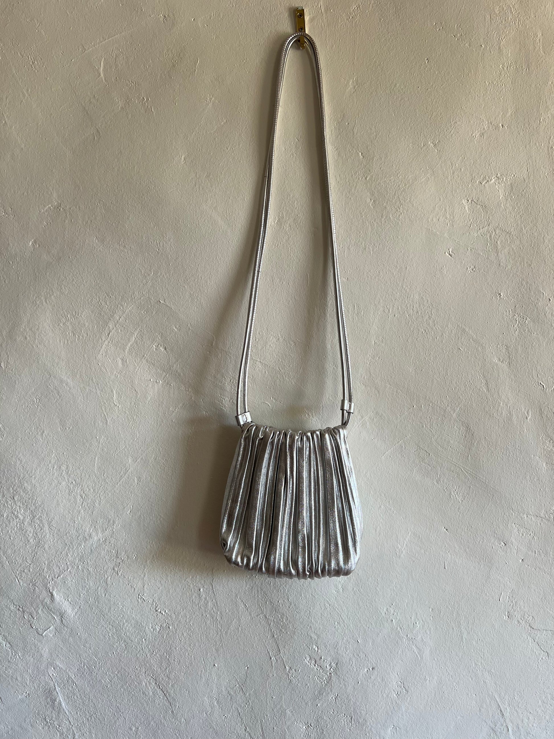 COS Silver Scallop Leather Crossbody Bag hanging against a white wall 