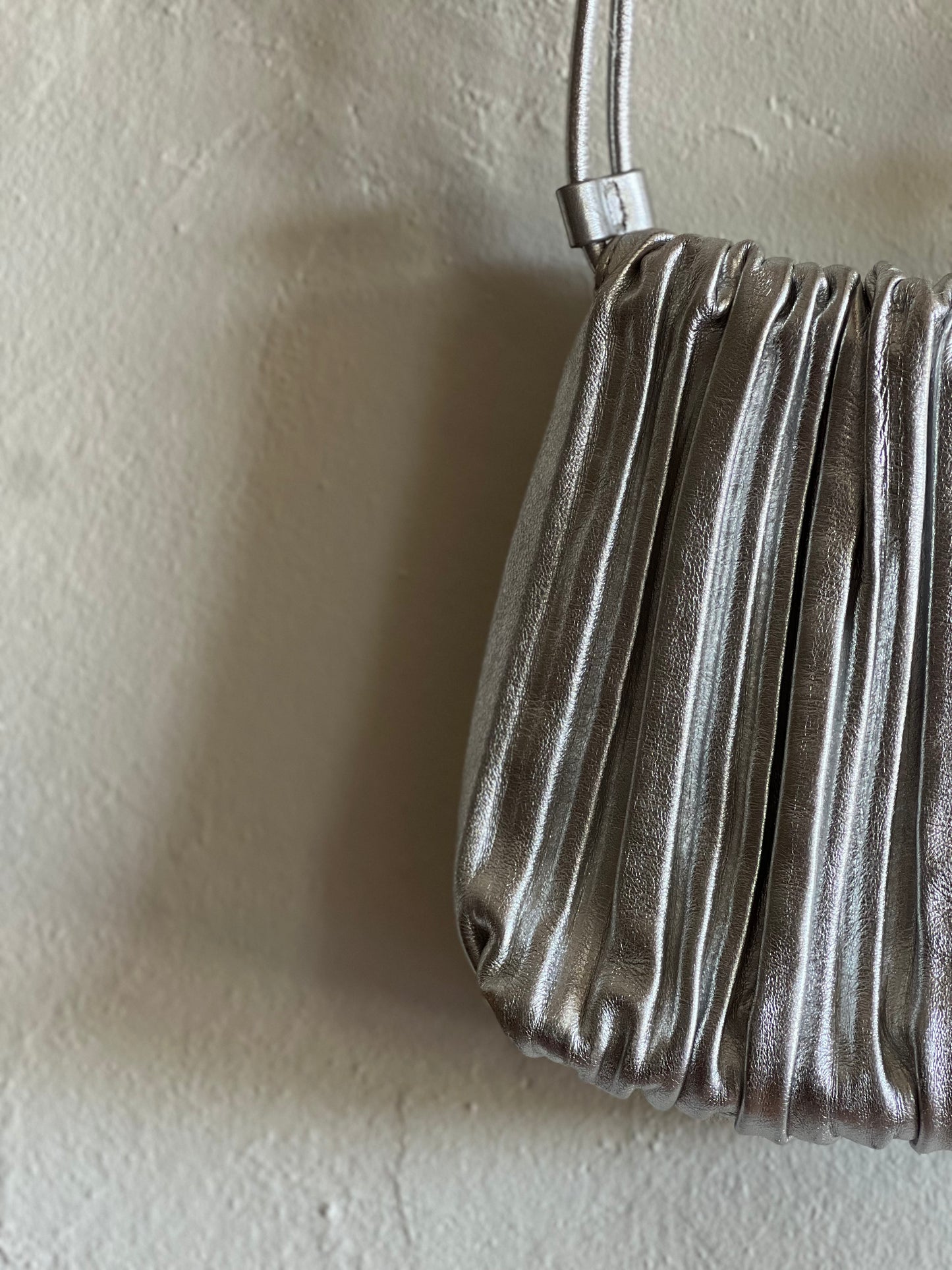 COS Silver Scallop Leather Crossbody Bag hanging against a white wall 