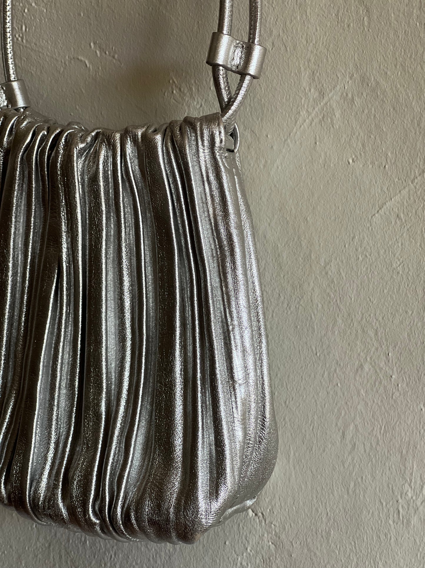 COS Silver Scallop Leather Crossbody Bag hanging against a white wall 