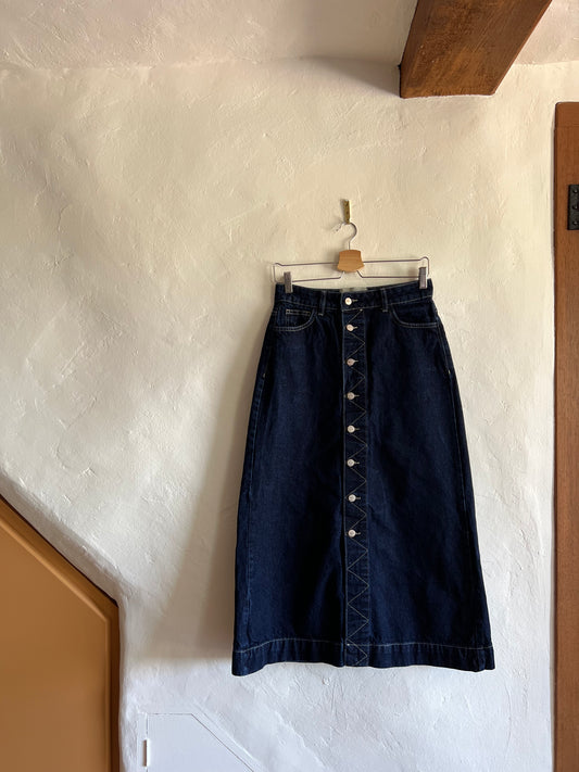 Damson Madder Dark Denim Midi Skirt hanging against a white wall 