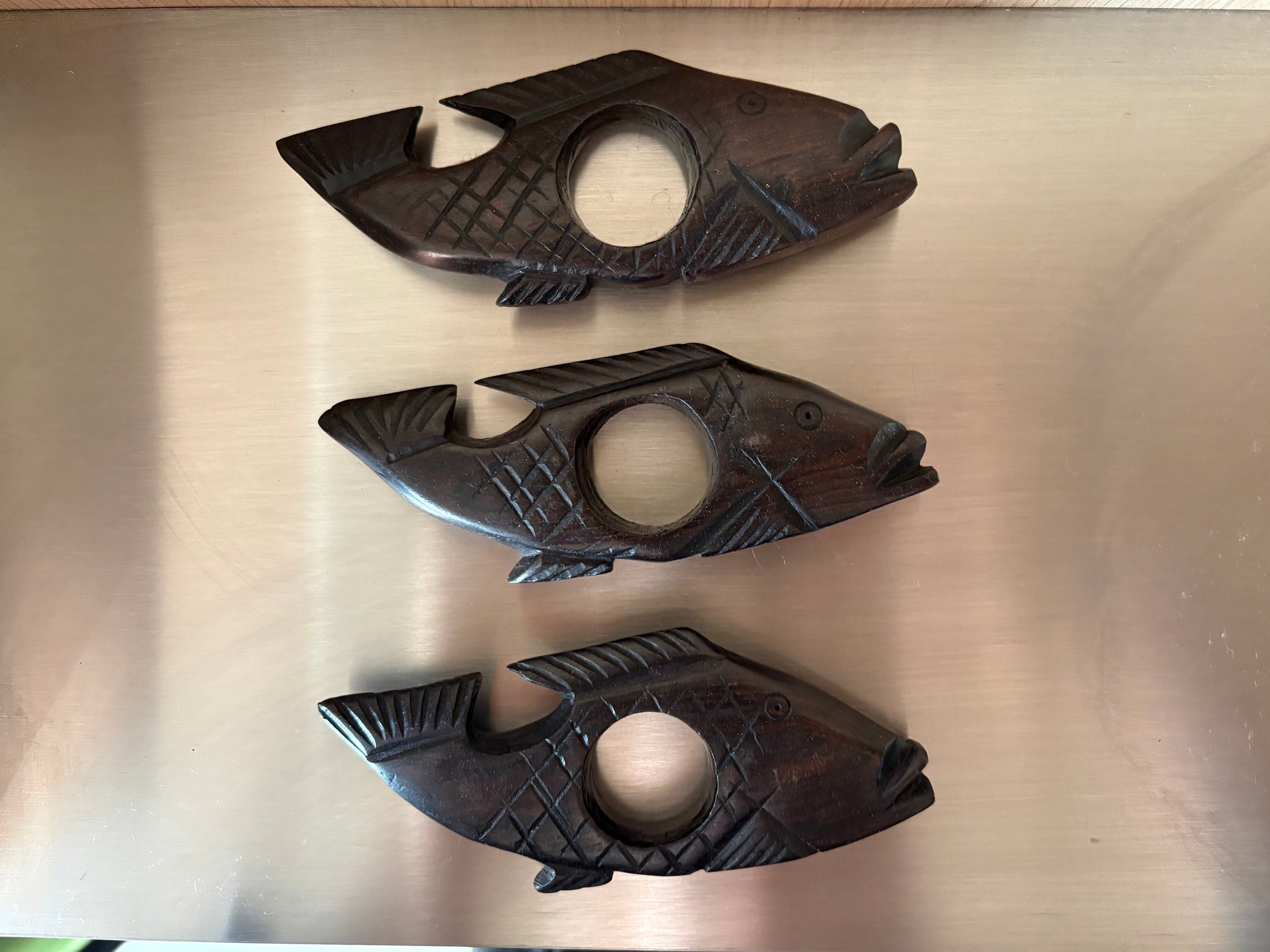Three wooden fish-shaped coasters on a metallic surface